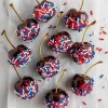 Chocolate-dipped cherries rolled in red, white, and blue sprinkles, drying on a sheet of parchment paper.
