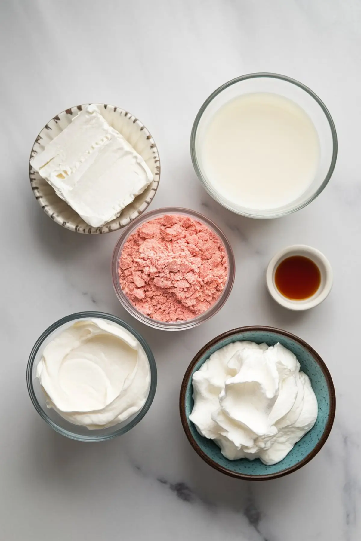 Top-down view of six dessert dip ingredients in separate bowls: cream cheese, strawberry cake mix, milk, whipped topping, sour cream, and vanilla extract, arranged on a white surface for a clean prep layout.