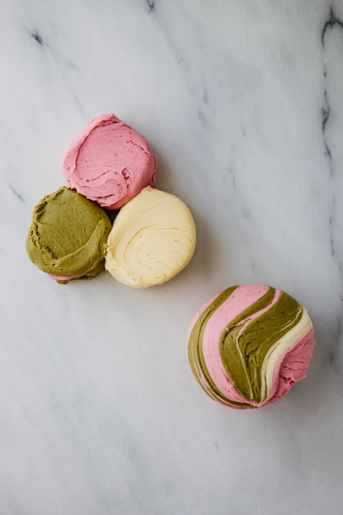 Four scoops of cookie dough—pink strawberry, green matcha, and beige vanilla—arranged to show individual colors and a combined marbled swirl dough ball on the side, ready for shaping.