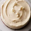 Overhead view of a frosted white chocolate cake topped with curled white chocolate shavings, highlighting the smooth swirl pattern in the frosting.