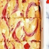Freshly baked white chocolate raspberry blondies in a baking dish lined with parchment paper, sliced into squares and topped with melted white chocolate chunks and bright raspberry swirls.