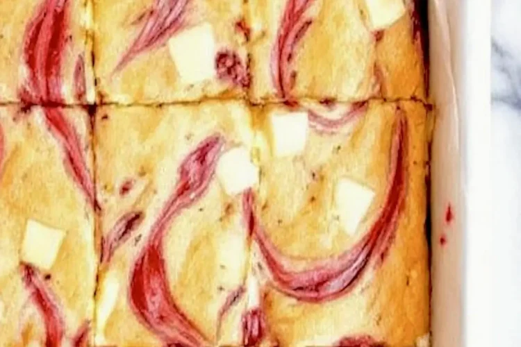 Freshly baked white chocolate raspberry blondies in a baking dish lined with parchment paper, sliced into squares and topped with melted white chocolate chunks and bright raspberry swirls.