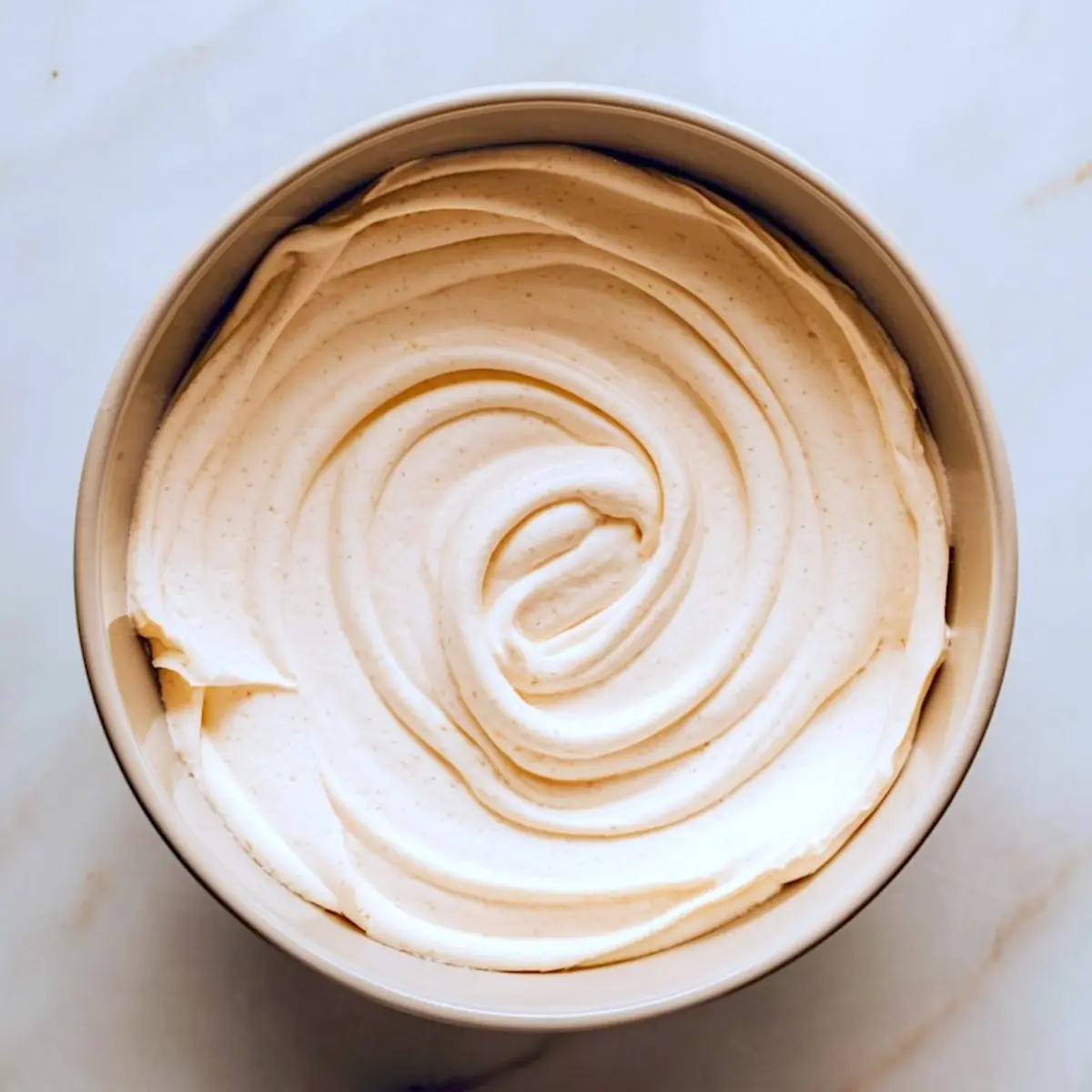Bowl of whipped cheesecake filling with smooth, creamy texture and subtle vanilla bean flecks, ready to be layered over brownie batter.
