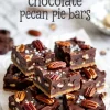 Salted dark chocolate pecan pie bars arranged on parchment paper, showcasing glossy chocolate tops, crunchy pecans, and coarse sea salt flakes, with a text overlay labeling the dessert.
