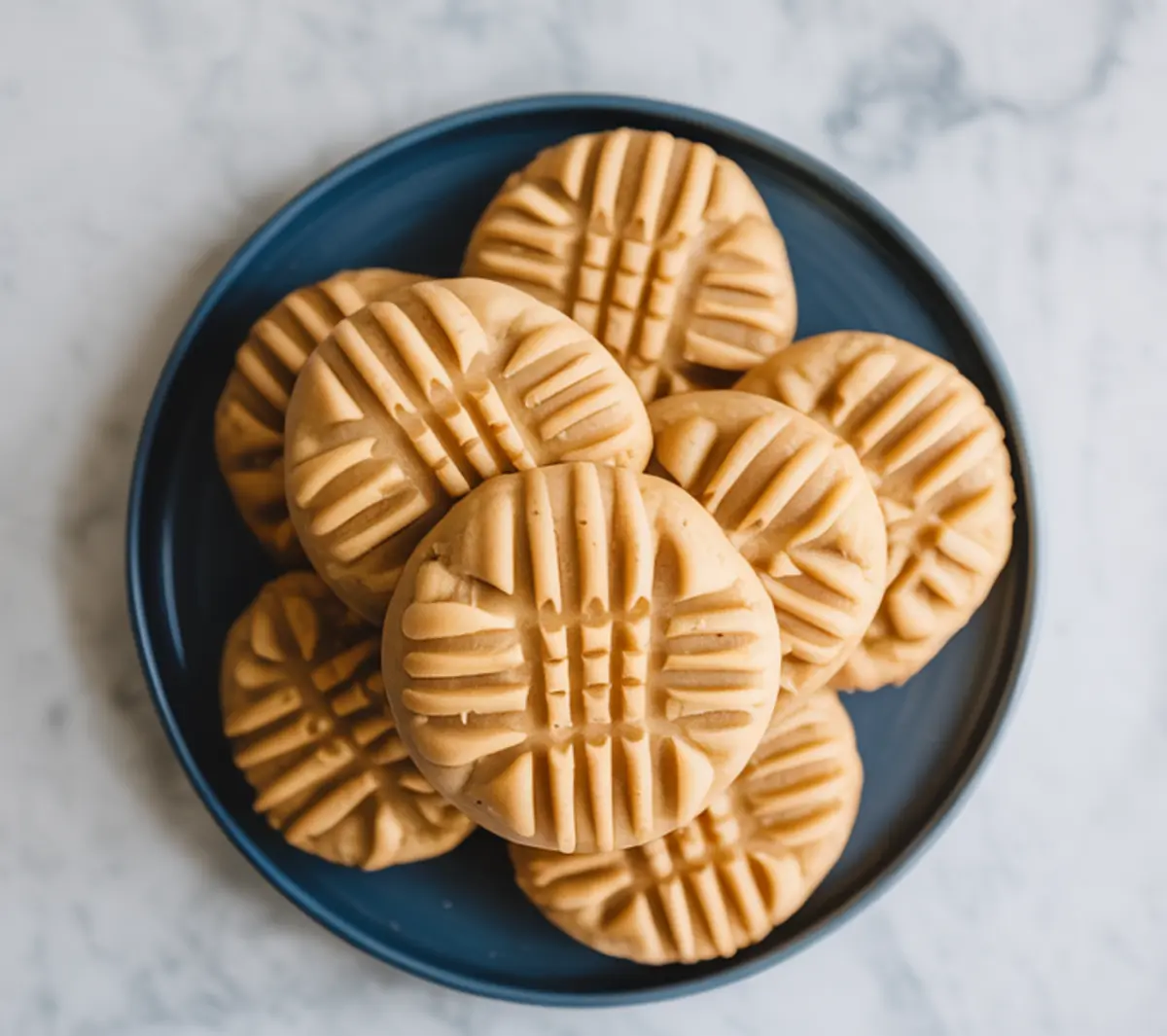 Blue plate stacked with baked peanut butter cookies showing a defined fork pattern on each. A clean, minimal image representing best ever peanut butter cookies for easy dessert recipes.