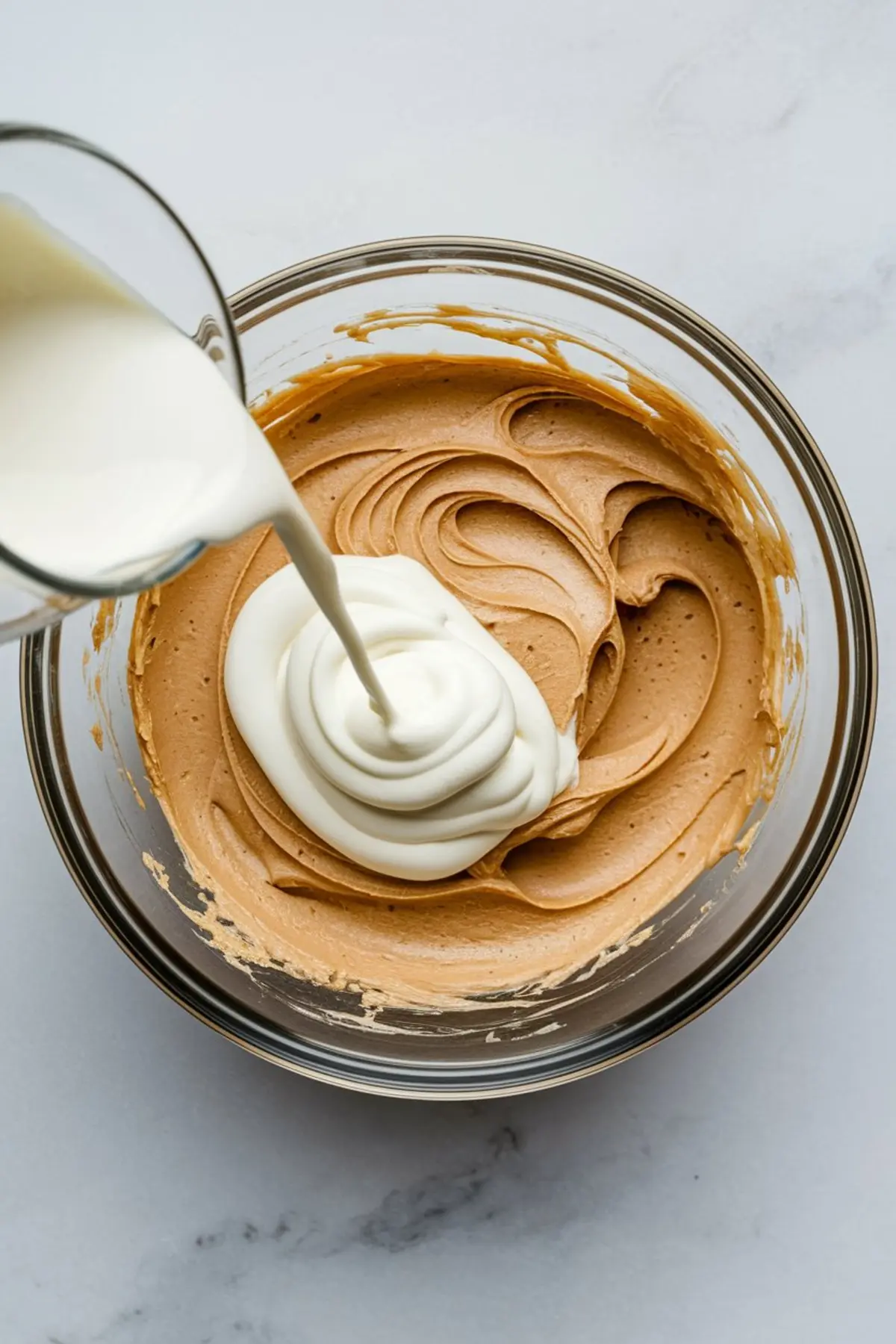 Pouring cream into a bowl of whipped peanut butter frosting, highlighting the mixing stage for a fluffy peanut butter buttercream used in peanut butter cake recipes or peanut butter icing for brownies.