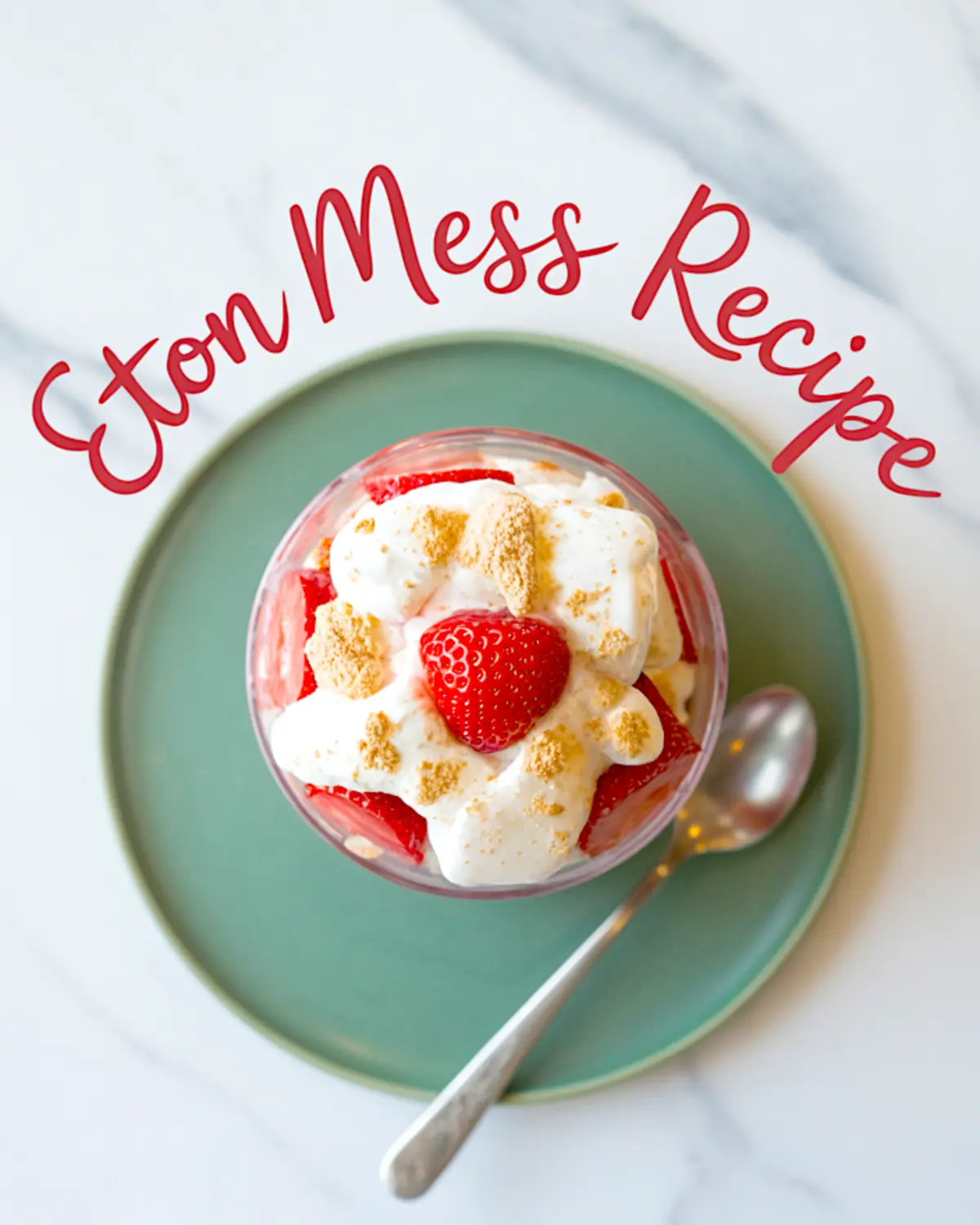 Top-down view of a glass filled with Eton Mess dessert, layered with whipped cream, fresh strawberries, and crushed meringue, styled on a green plate with a spoon on a marble surface.
