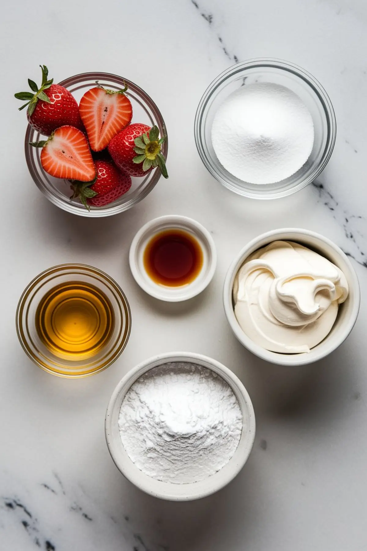 Flat lay of Eton Mess ingredients including halved strawberries, granulated sugar, vanilla extract, whipped cream, honey, and powdered sugar in individual bowls on a marble surface.
