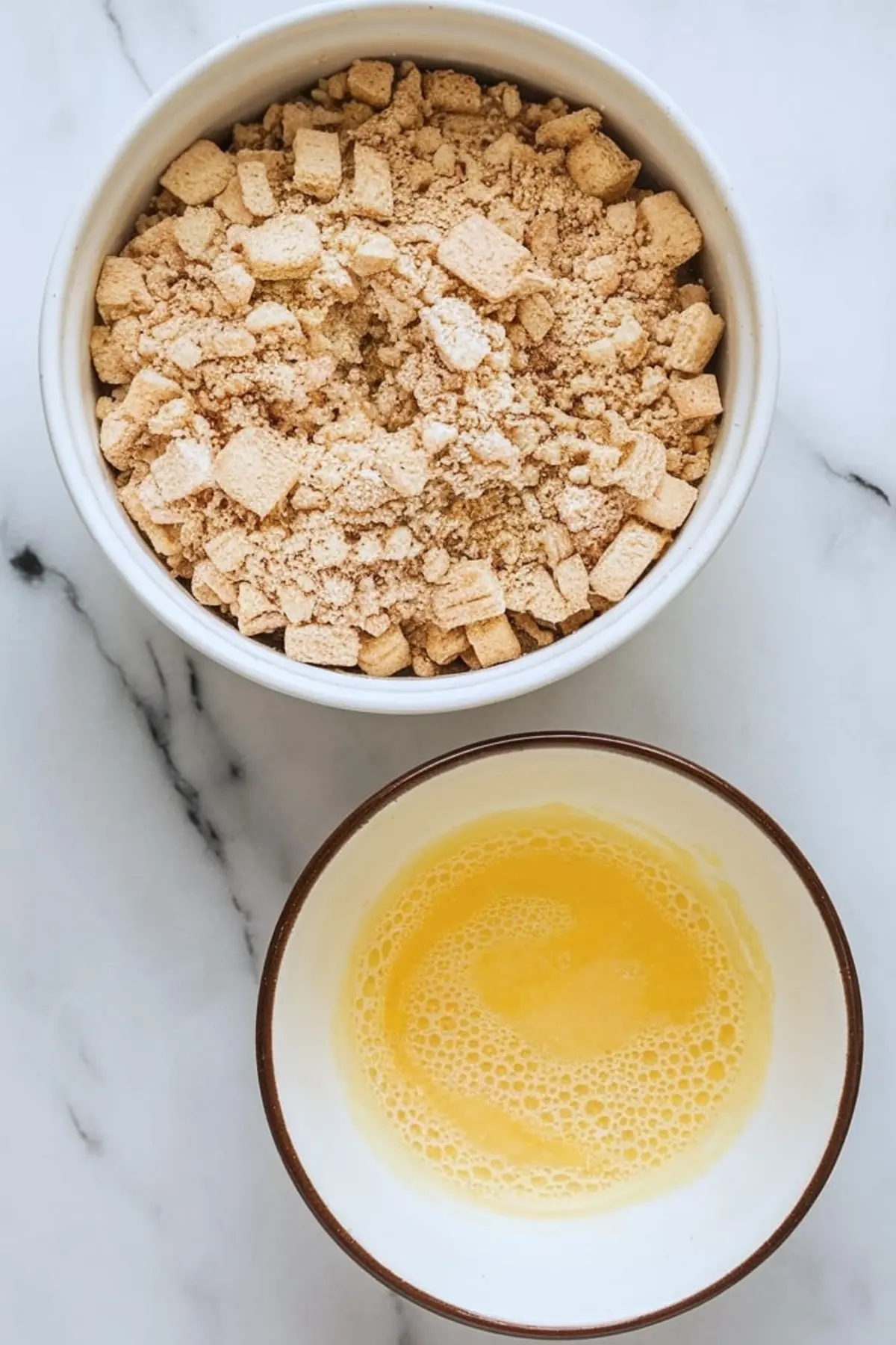 Flat lay of a bowl filled with crushed vanilla cookies and a second bowl with frothy lemon mixture on a marble surface, used for frozen lemon soufflé base.
