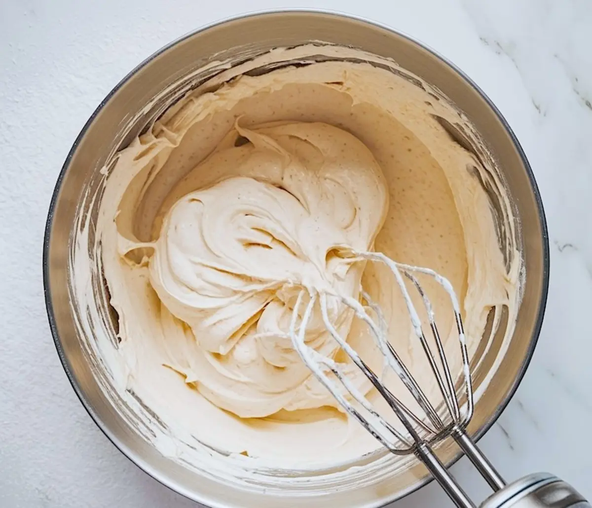Creamy pecan pie filling in a mixing bowl with a hand mixer, showing smooth whipped texture for the no-bake dessert layer.