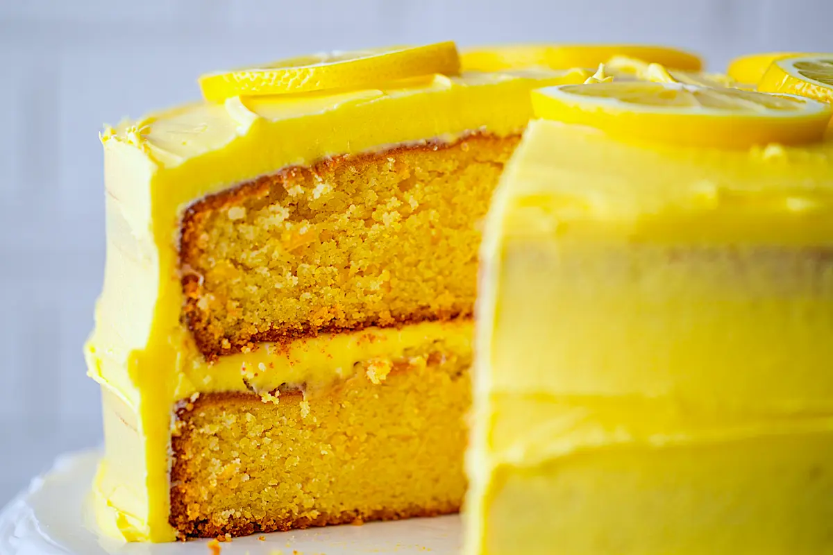Sliced lemon cake with moist yellow crumb and thick buttercream frosting, topped with fresh lemon slices.