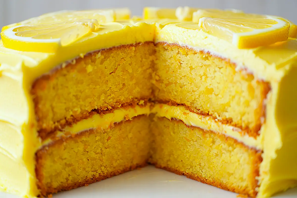 Cross-section of a layered lemon cake revealing dense, moist texture and vibrant yellow frosting between layers, topped with lemon slices.