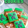 Plate of Minecraft sugar cookies decorated with Creeper faces and pixel grass block designs, arranged on a white plate over a marble countertop, with bold green “Minecraft Cookies” text above.