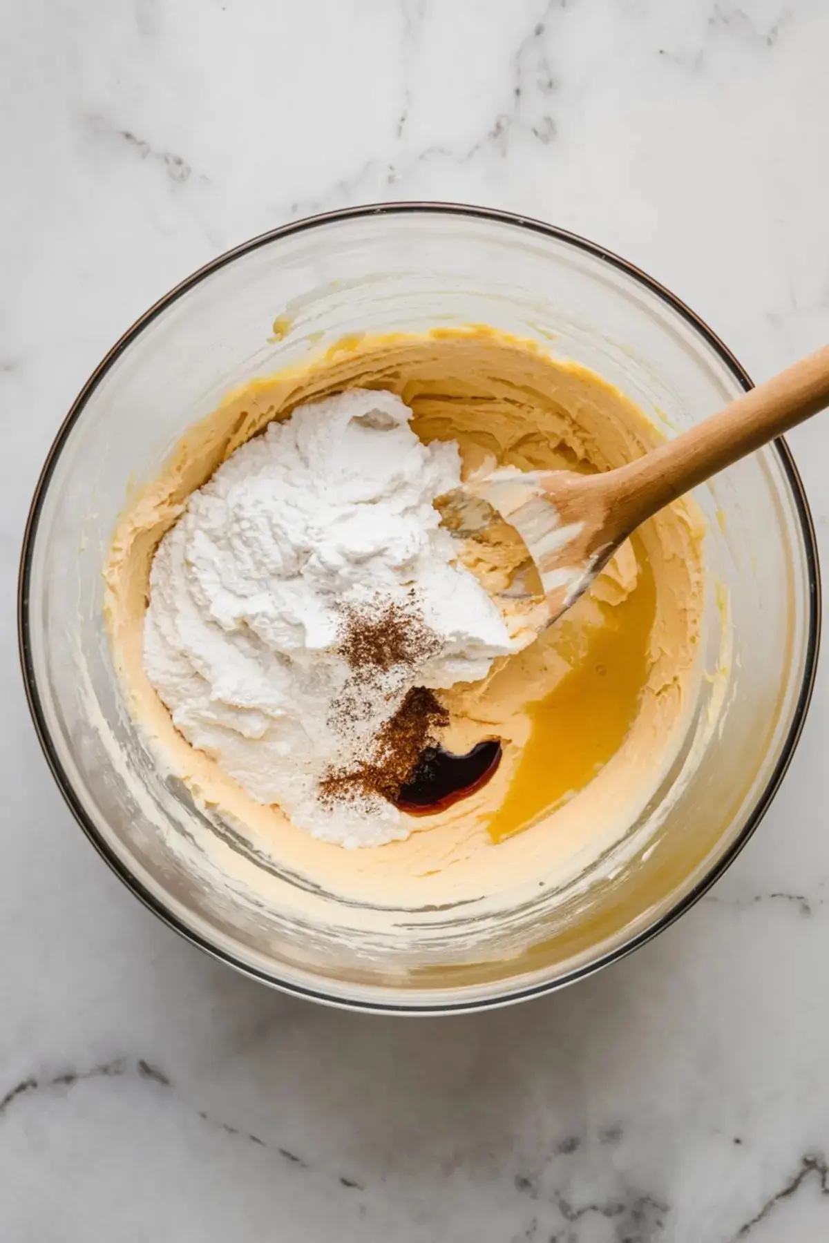 Cream cheese filling being mixed in a bowl with powdered sugar, vanilla extract, and ground spices for a rich cheesecake mixture.