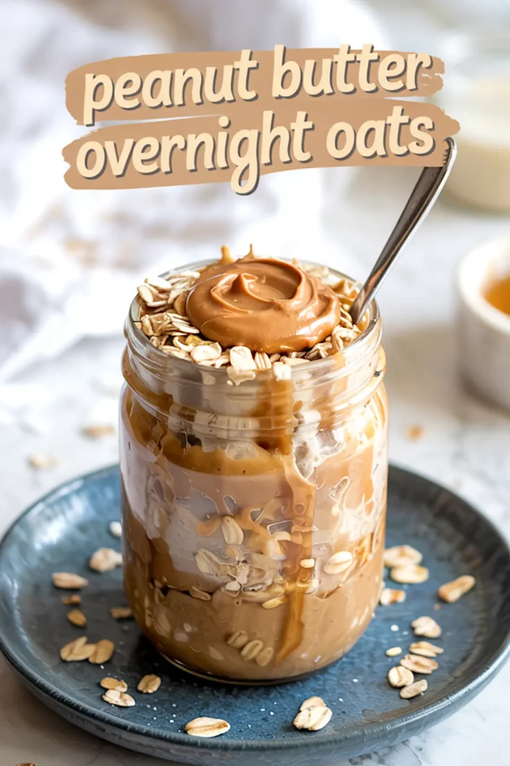 Mason jar filled with layered peanut butter overnight oats, oats on top with a swirl of peanut butter, and text overlay reading “peanut butter overnight oats.” Placed on a blue plate with oats scattered. Great for over night oats in a jar and protein overnight oats healthy content.