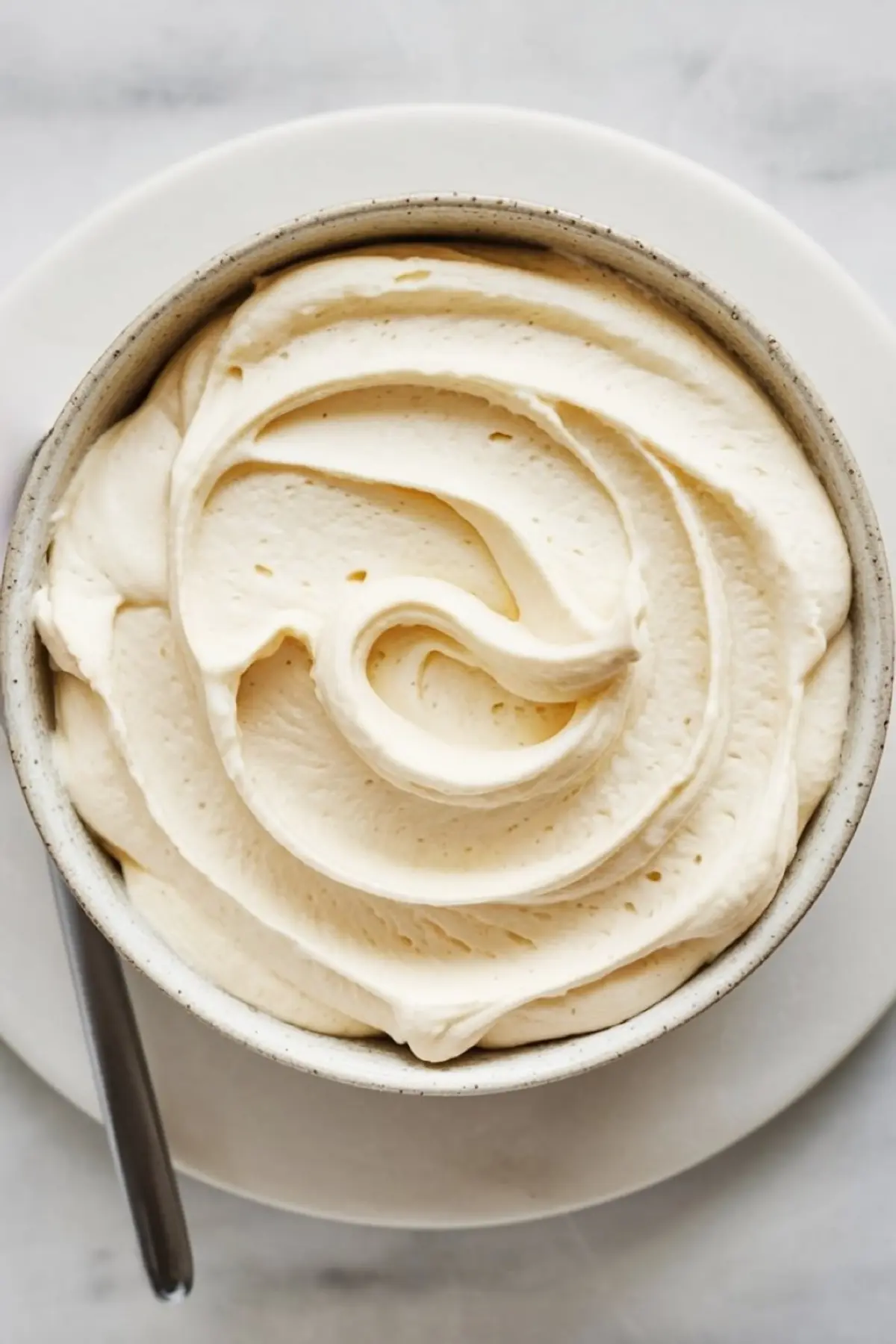 Bowl of whipped cream cheese frosting with a smooth, swirled texture, ready for decorating cakes and cupcakes.