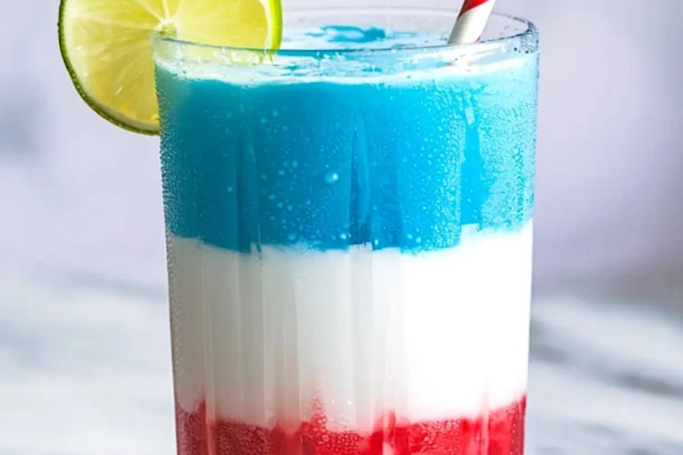 Close-up of a vibrant red, white, and blue slushie in a tall glass with a lime slice and striped paper straw, condensation on the glass highlighting the icy texture, placed on a white marble surface.