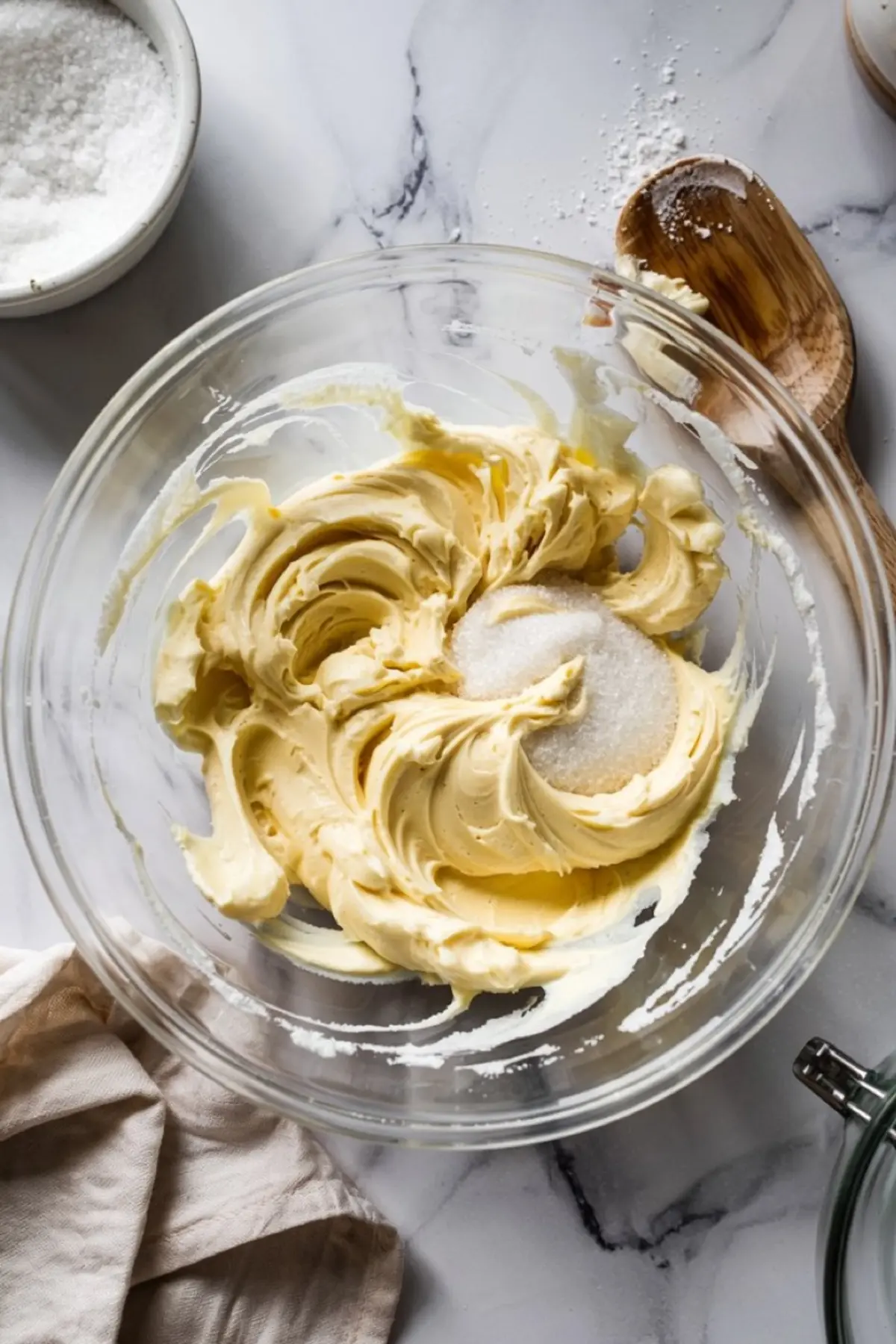 Creamed butter and sugar mixture swirled in a glass bowl with a smooth, fluffy texture, surrounded by baking tools on a white marble surface.