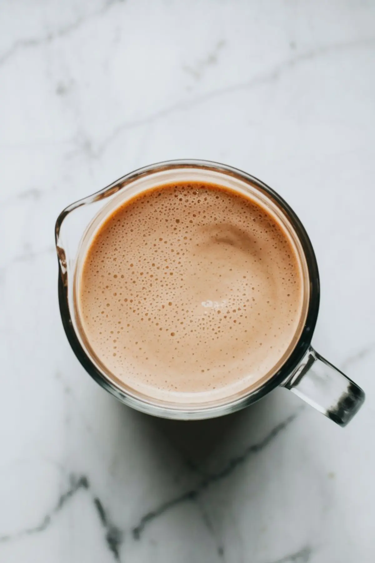 Creamy banana peanut butter smoothie blended to a smooth consistency inside a clear glass blender jar, placed on a marble countertop.