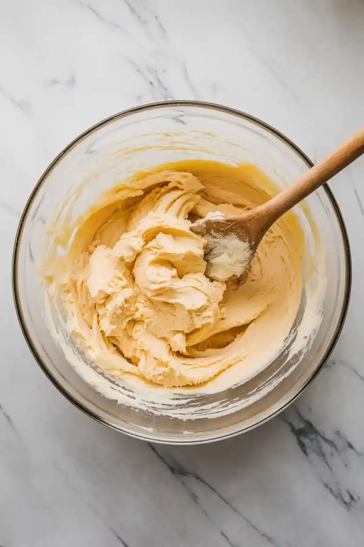 Thick vanilla pastry cream filling in a glass bowl with a wooden spoon, freshly whipped and ready to fill Boston cream pie cupcakes.