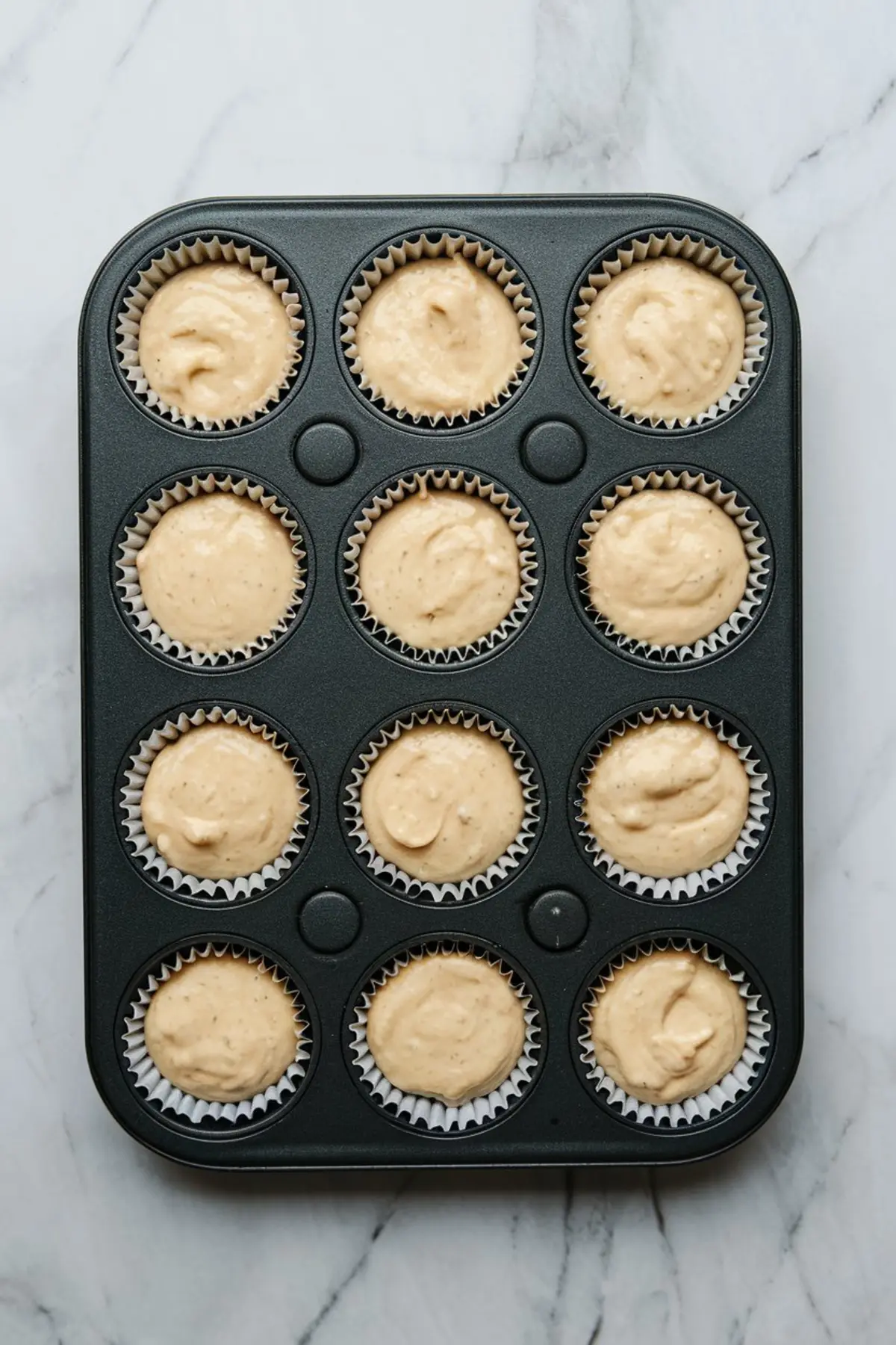 Muffin pan filled with cupcake liners and vanilla batter, ready to bake Boston cream pie cupcakes with a light and fluffy texture.