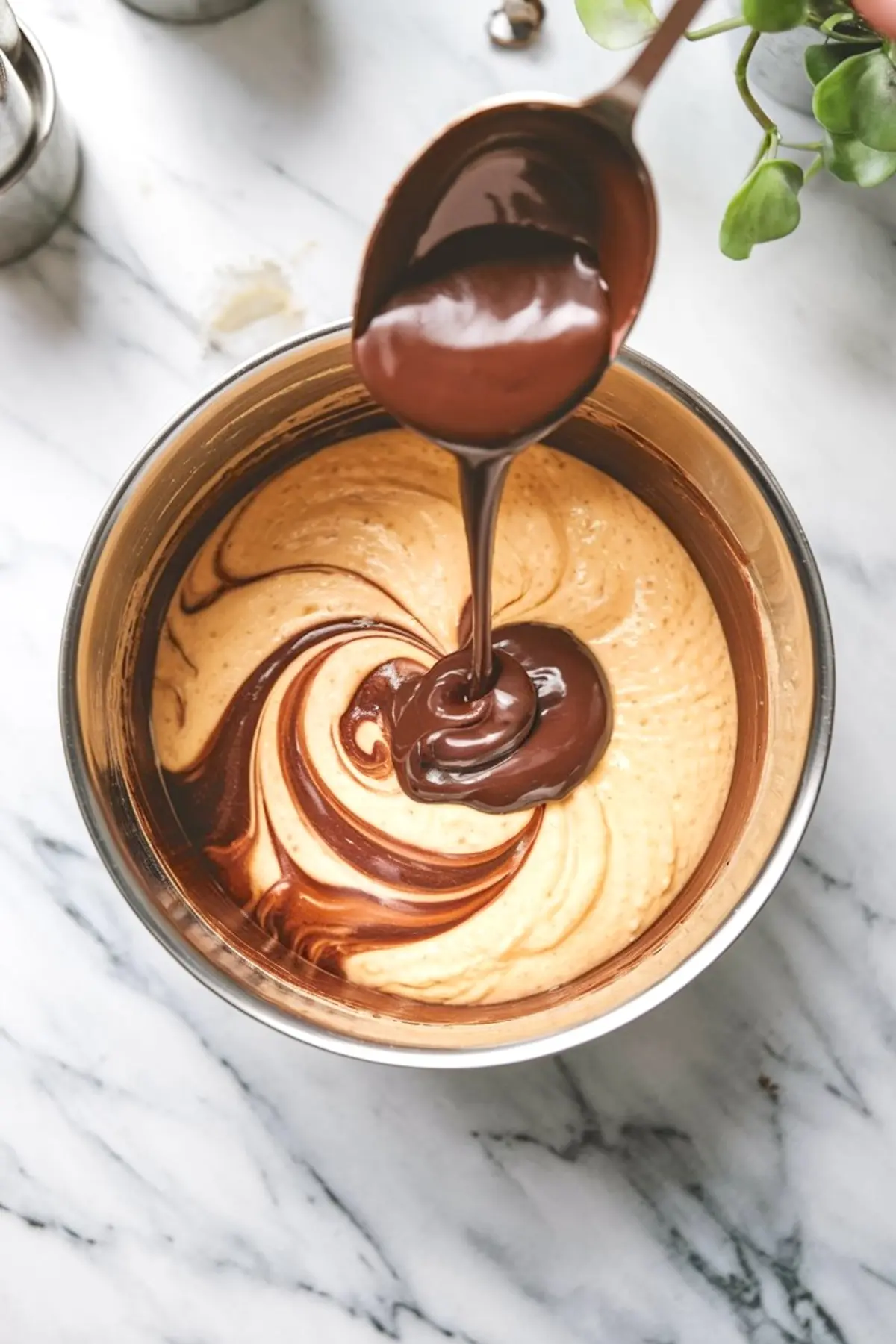 Silky melted chocolate streams from a spoon into light batter, forming marbled swirls in a metal bowl for brownie crinkle cookie dough.