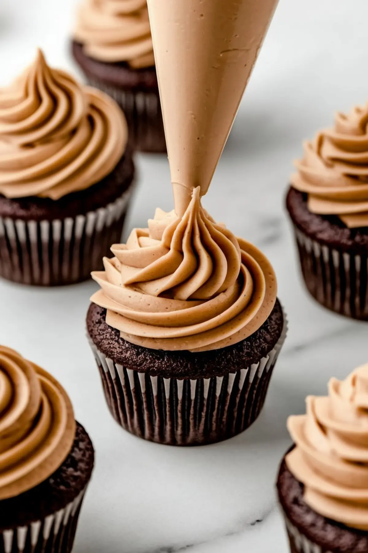 Piping creamy peanut butter frosting onto chocolate cupcakes, creating smooth swirls, demonstrating techniques for chocolate peanut butter frosting and peanut butter muffins recipes.