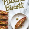 Chocolate pistachio biscotti slices arranged on marble background. The text “Pistachio Biscotti” is written above the cookies. A white plate with a single biscotti slice and scattered pistachios are placed beside.