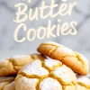 Stack of golden gooey butter cookies on a blue plate, dusted with powdered sugar and cracked on top, styled in front of a light marble background with handwritten recipe title overlay.