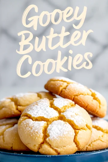 Stack of golden gooey butter cookies on a blue plate, dusted with powdered sugar and cracked on top, styled in front of a light marble background with handwritten recipe title overlay.
