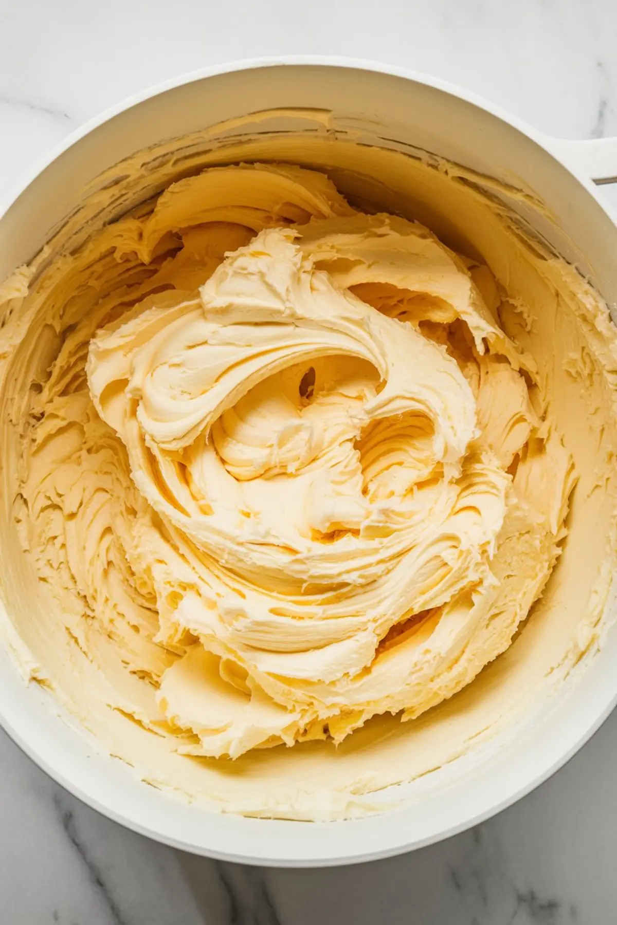 Close-up of whipped lemon frosting in a large mixing bowl with thick, airy swirls, showcasing its creamy and fluffy texture.
