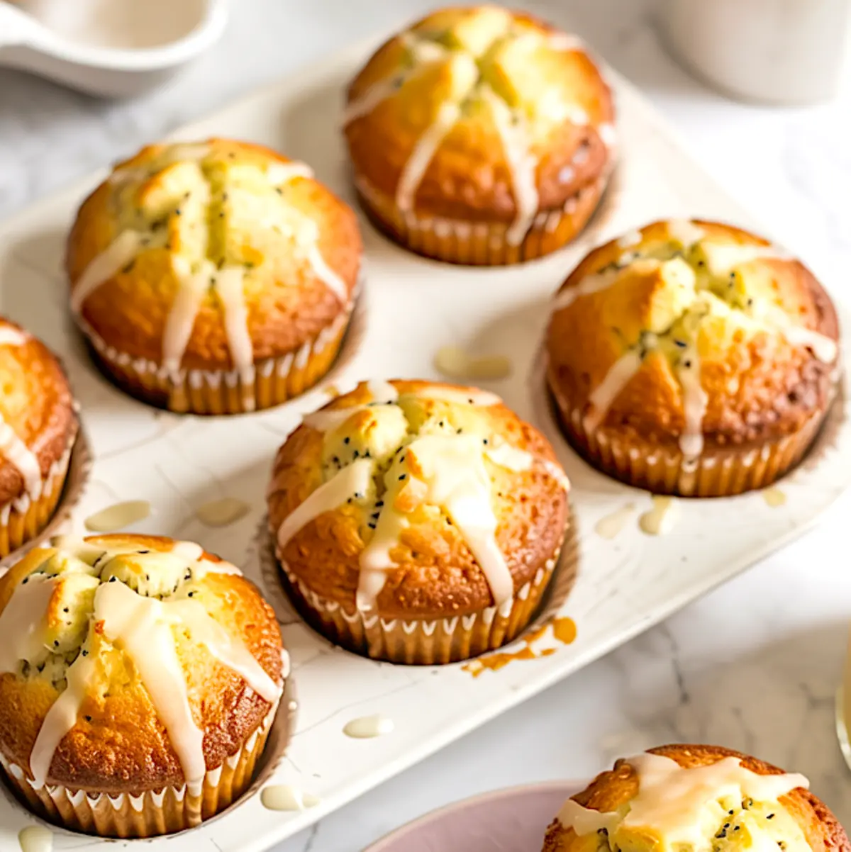 Glazed lemon poppy seed muffins in a white muffin tin, golden brown and topped with drizzled icing.