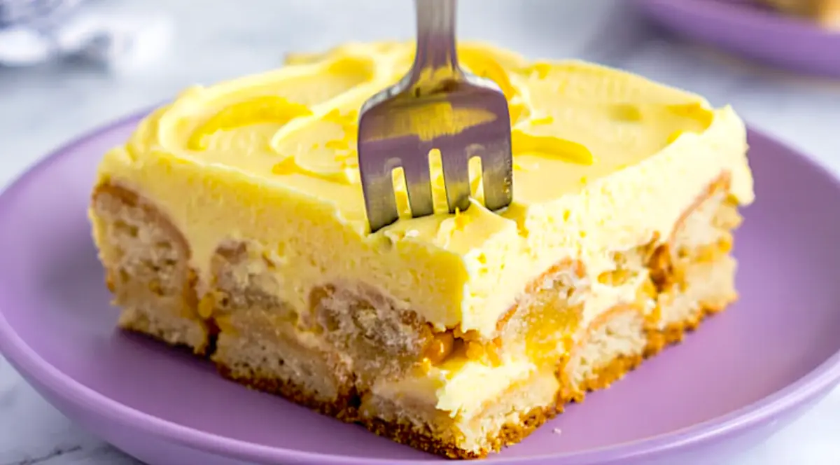 Close-up of a single slice of lemon tiramisu on a purple plate with a fork pressed into the creamy top, highlighting the layered texture and vibrant yellow lemon filling.