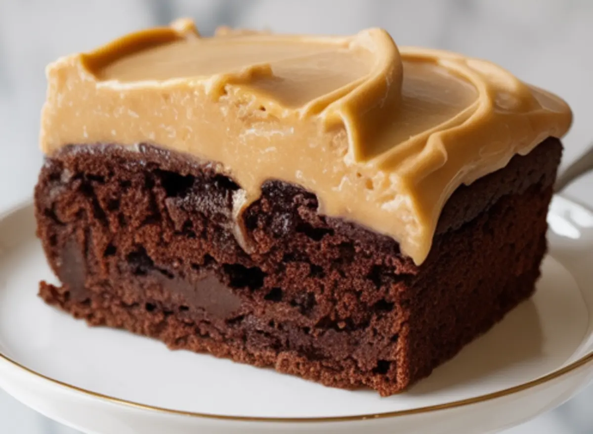 Close-up of a single slice of chocolate peanut butter cake on a white plate with gold trim. The slice shows moist chocolate cake with a thick layer of peanut butter frosting and rich chocolate filling.
