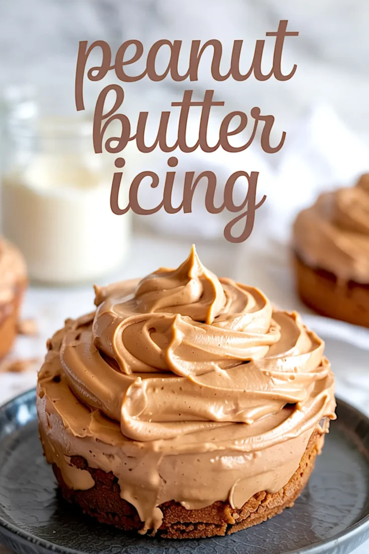 Peanut butter icing generously swirled on top of a small round cake, with text overlay reading “peanut butter icing” and blurred milk jar and additional cakes in the background.