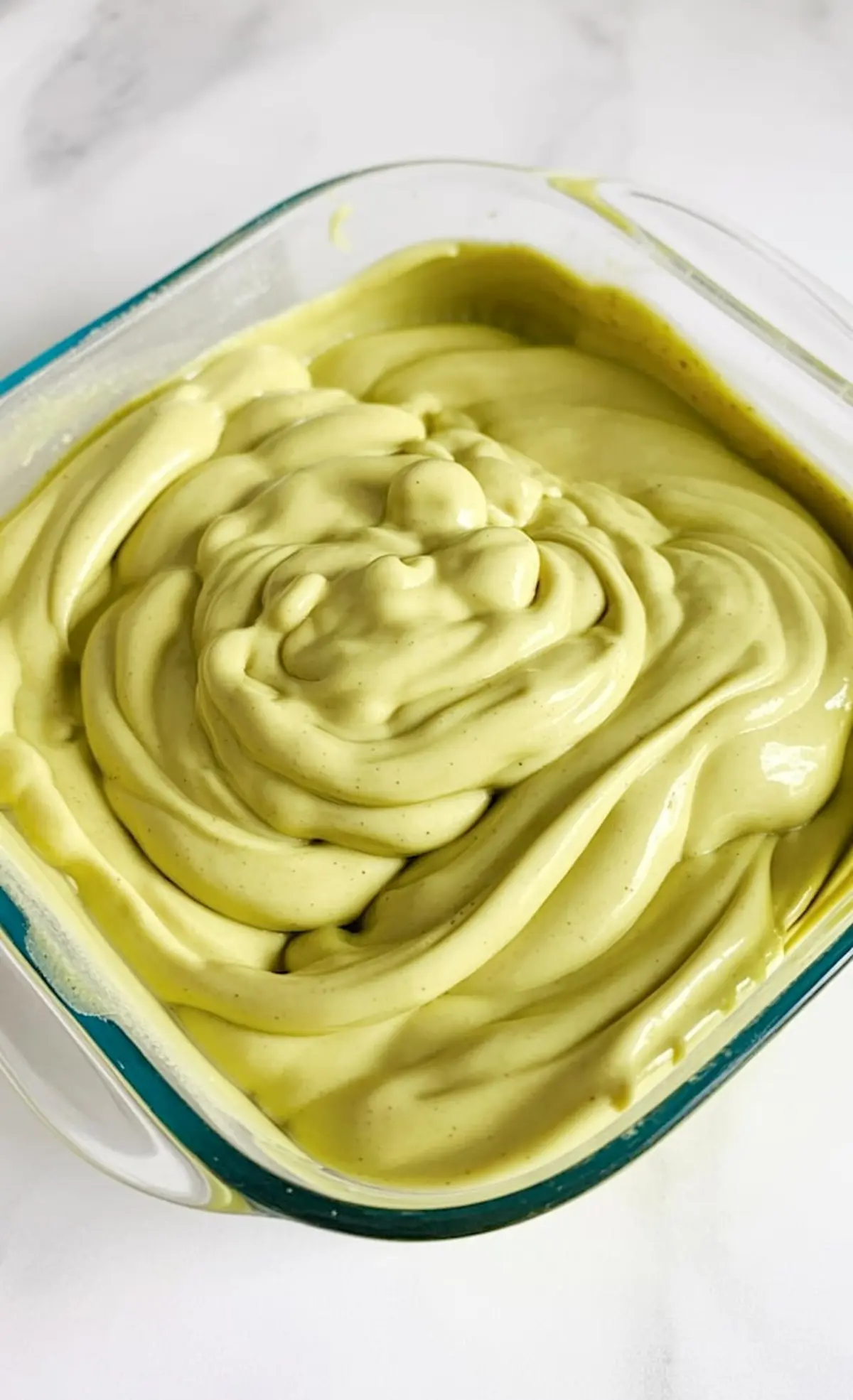 Glass dish filled with thick, swirled pistachio brigadeiro mixture in a pale green hue, ready to be shaped into truffles.
