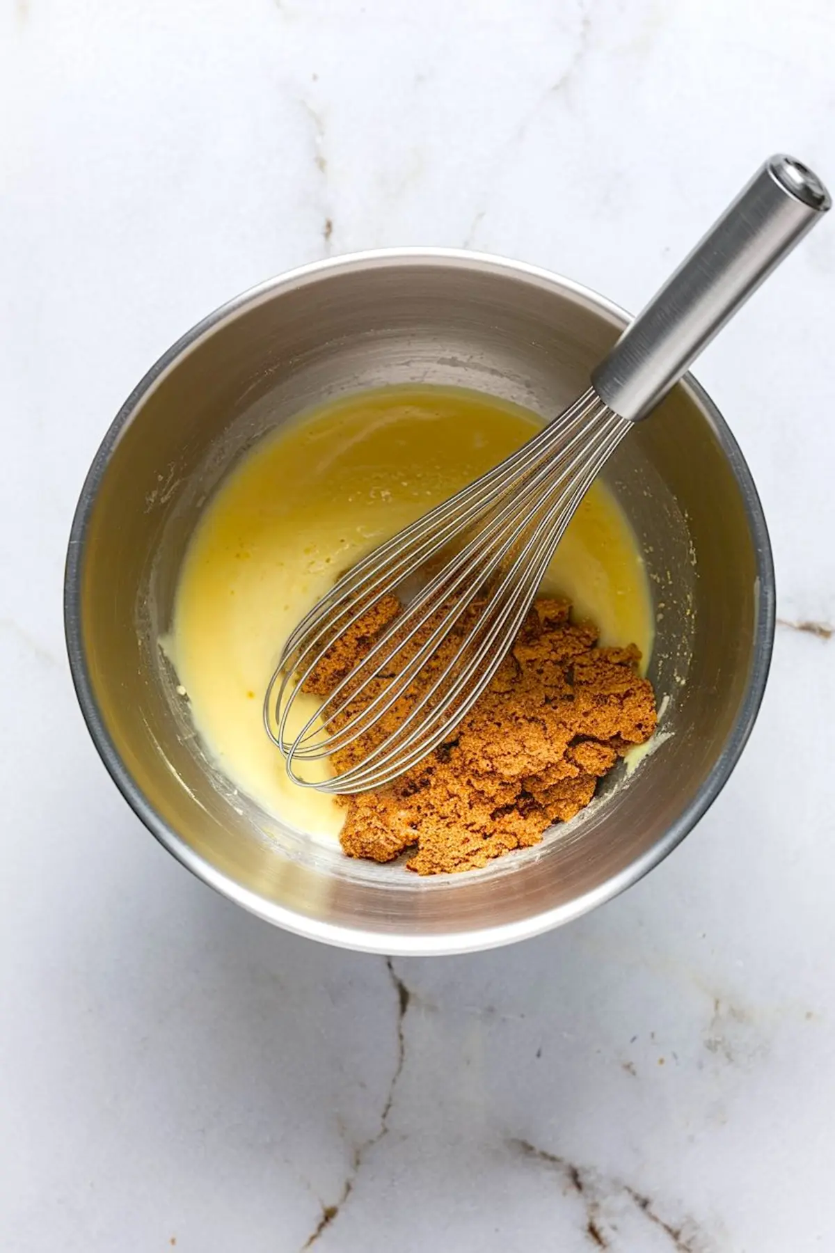Whisk blending melted butter and brown sugar in a stainless steel mixing bowl as part of the blondie batter preparation.
