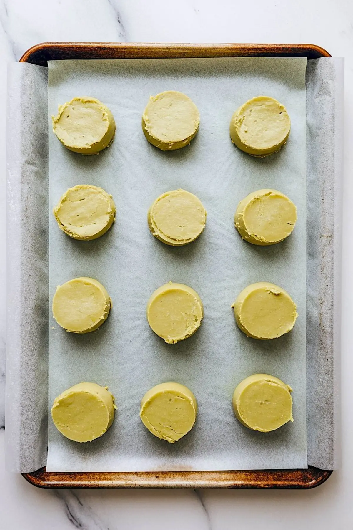 Raw pistachio cookie dough rounds neatly spaced on a parchment-lined baking tray, ready to bake.
