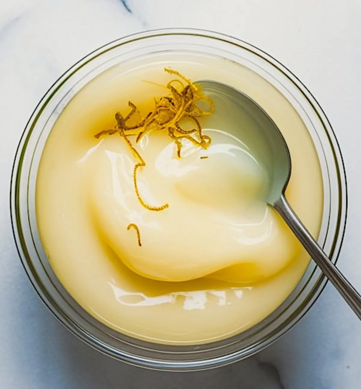 Small bowl of lemon glaze with zest curls on top, ready for drizzling over pistachio ricotta cookies.