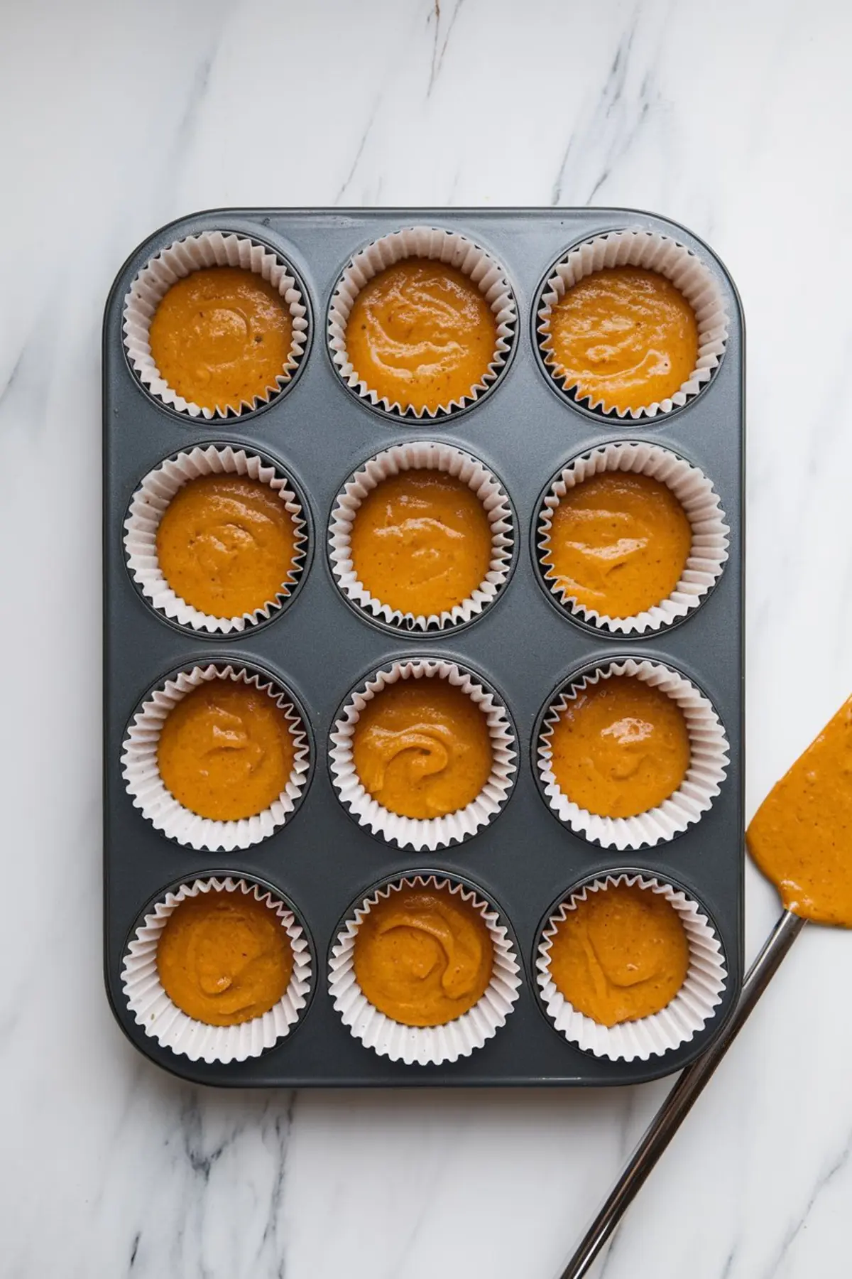 Unbaked pumpkin cupcake batter portioned into a nonstick muffin tin lined with white paper cups, ready for the oven.