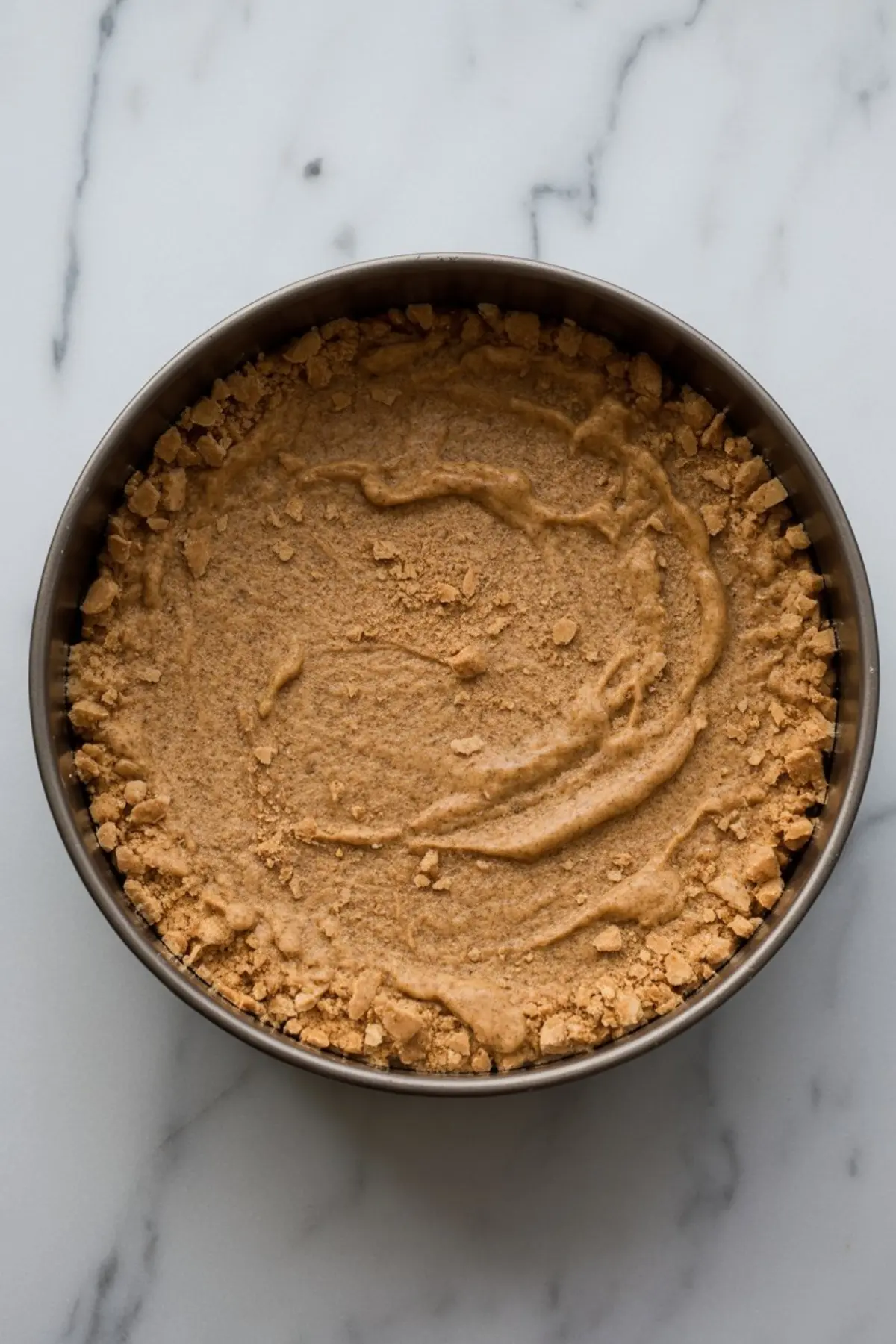 Close-up of a pressed graham cracker crust inside a round springform pan, ready for no-bake cheesecake filling. This preparation step highlights cheesecake design ideas and base preparation techniques for decorated cheesecake.
