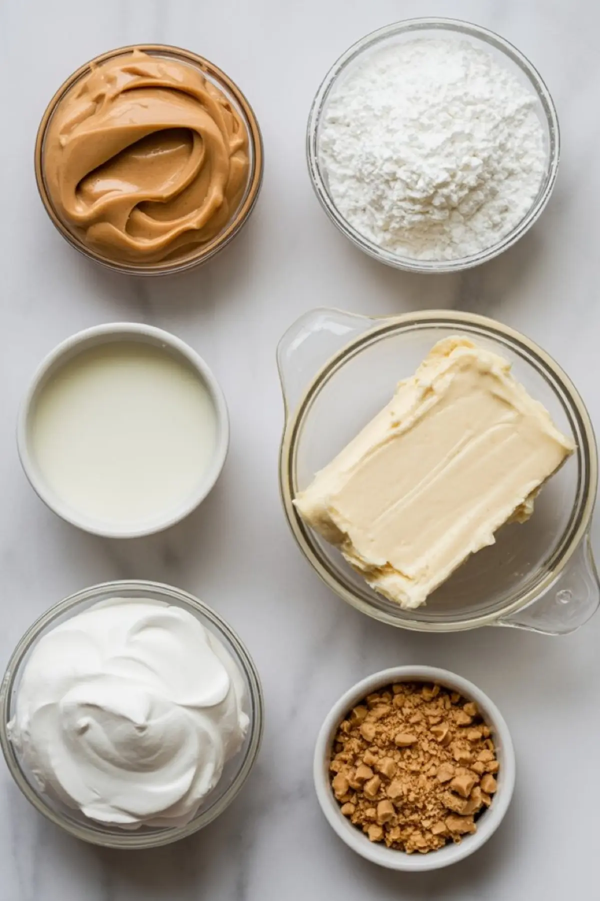Overhead view of peanut butter pie ingredients including creamy peanut butter, powdered sugar, milk, butter, whipped topping, and crushed peanut butter candy pieces.
