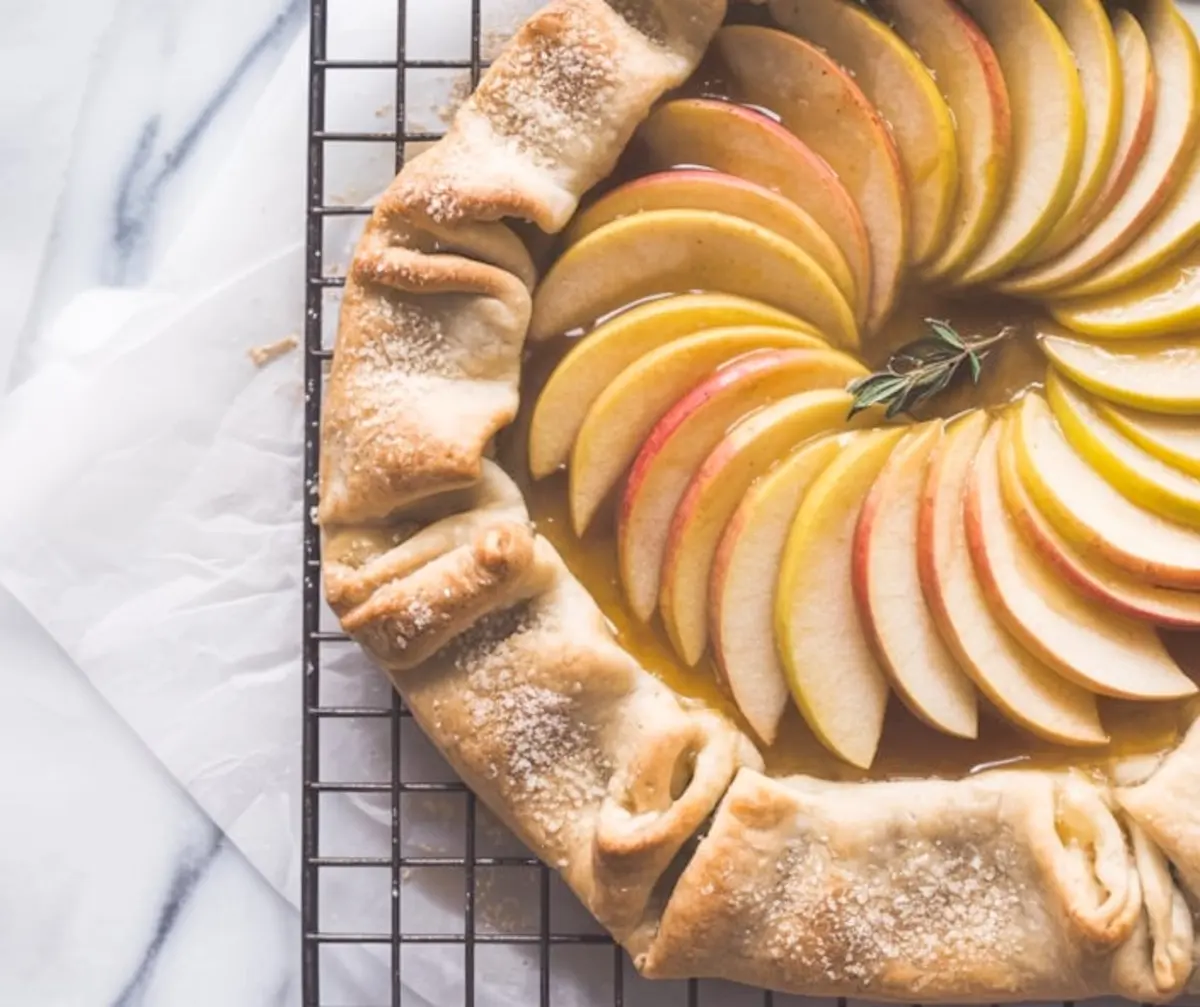 Golden apple galette topped with thinly sliced apples arranged in a spiral pattern on a flaky crust, baked until golden and dusted with sugar.