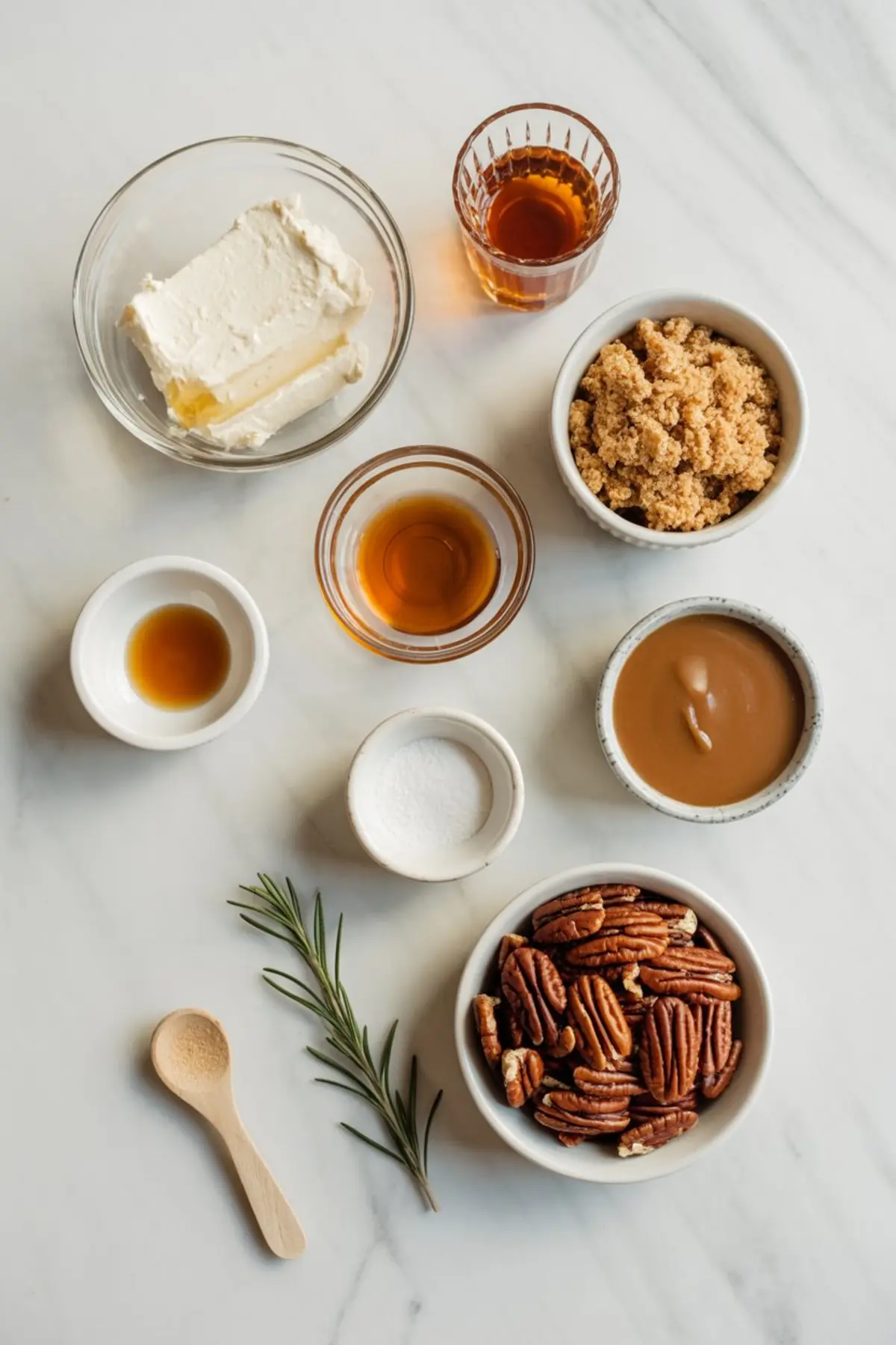 Flat lay of bourbon pecan pie dip ingredients including cream cheese, pecans, brown sugar, caramel sauce, bourbon, vanilla extract, salt, and fresh rosemary on a marble surface.
