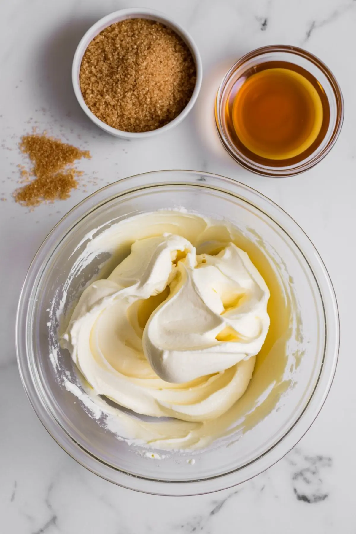 Creamy whipped filling in a glass bowl with brown sugar and bourbon on the side, ready for making bourbon pecan pie dip.
