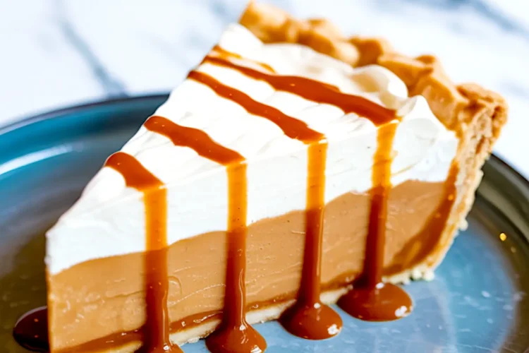 Slice of butterscotch pie with whipped cream and caramel drizzle on a blue plate, showing layers of creamy filling and crisp crust.