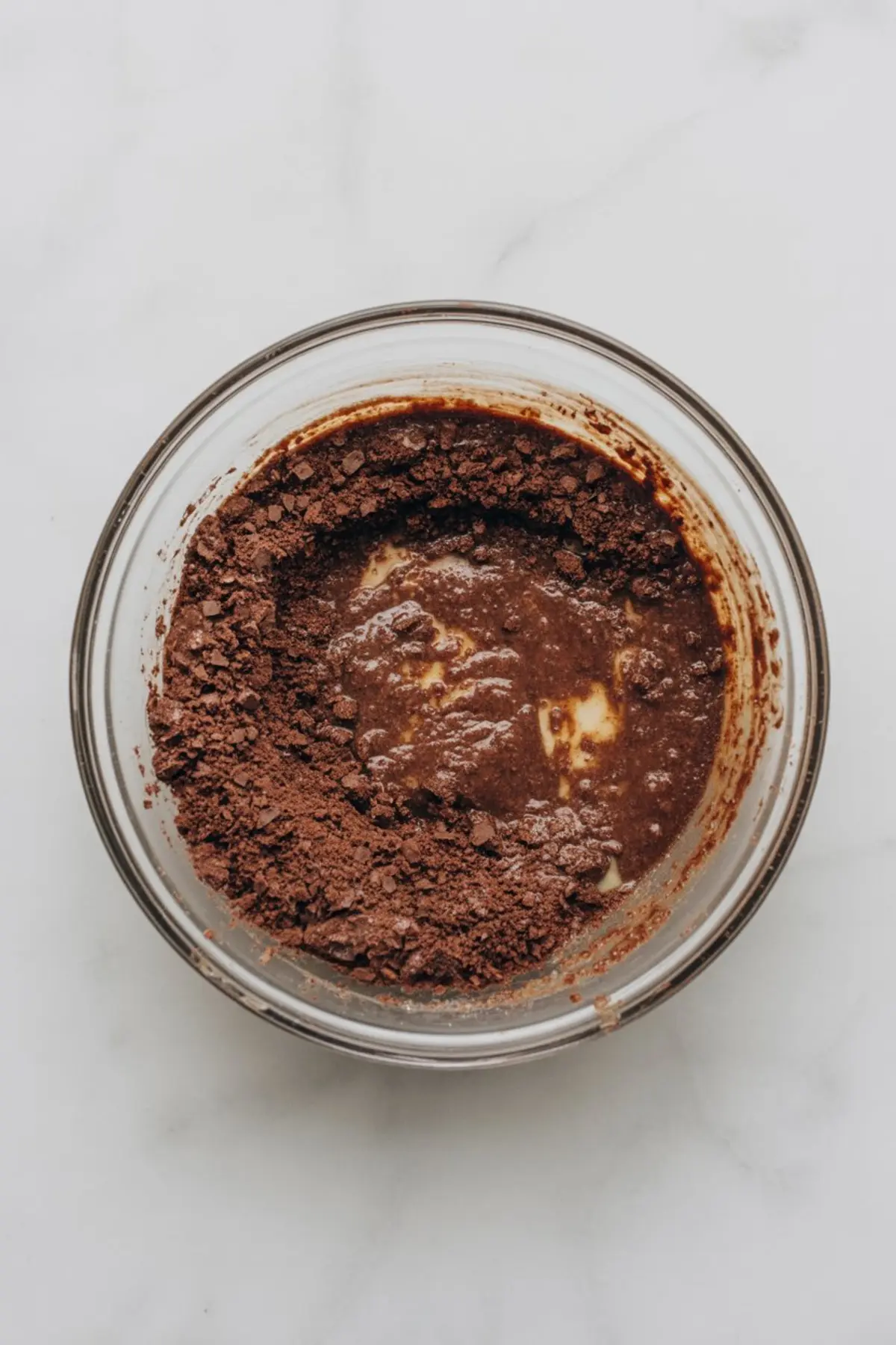 Mixing bowl filled with partially combined crushed chocolate cookies, butter, and sweetened condensed milk to make a pie crust base.