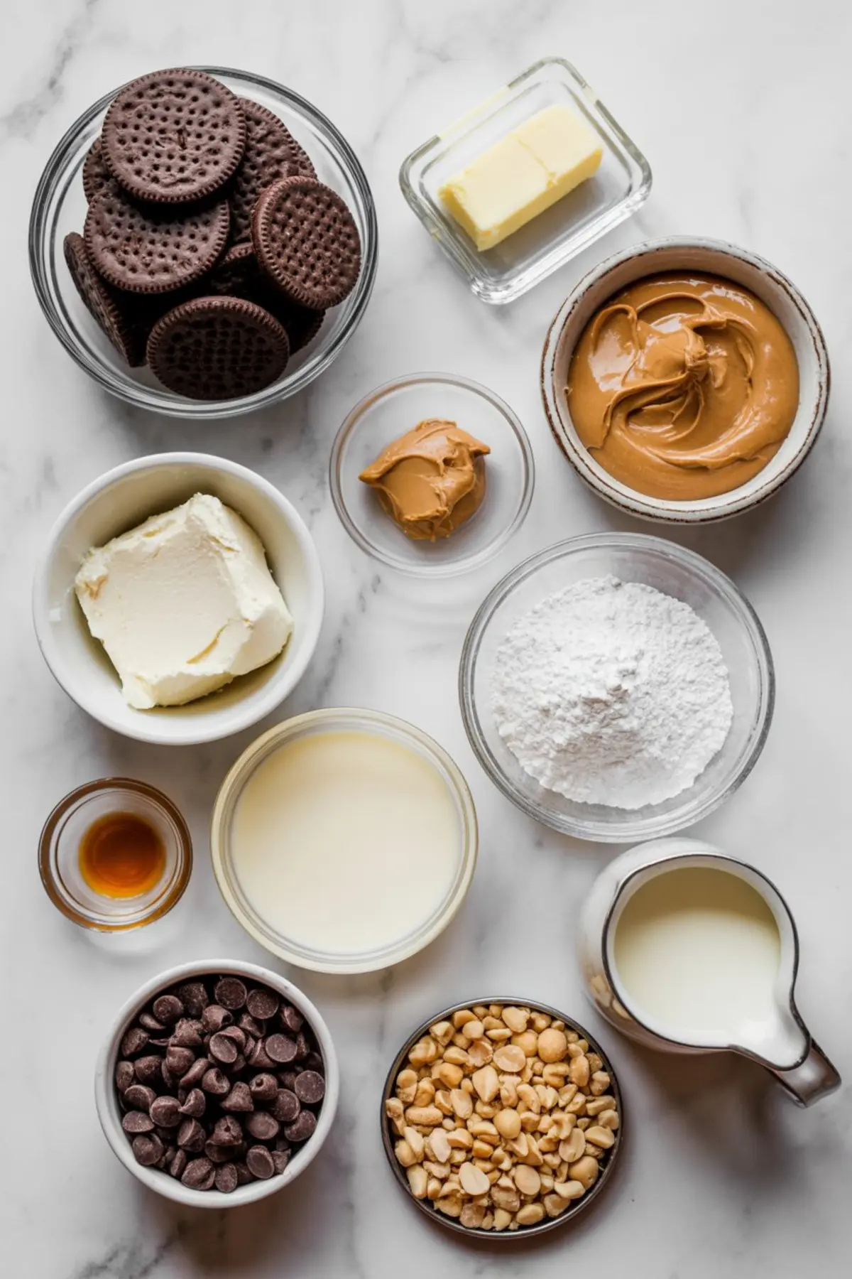 Overhead view of baking ingredients for chocolate peanut butter pie including sandwich cookies, butter, cream cheese, peanut butter, powdered sugar, chocolate chips, peanuts, vanilla, milk, and sweetened condensed milk.