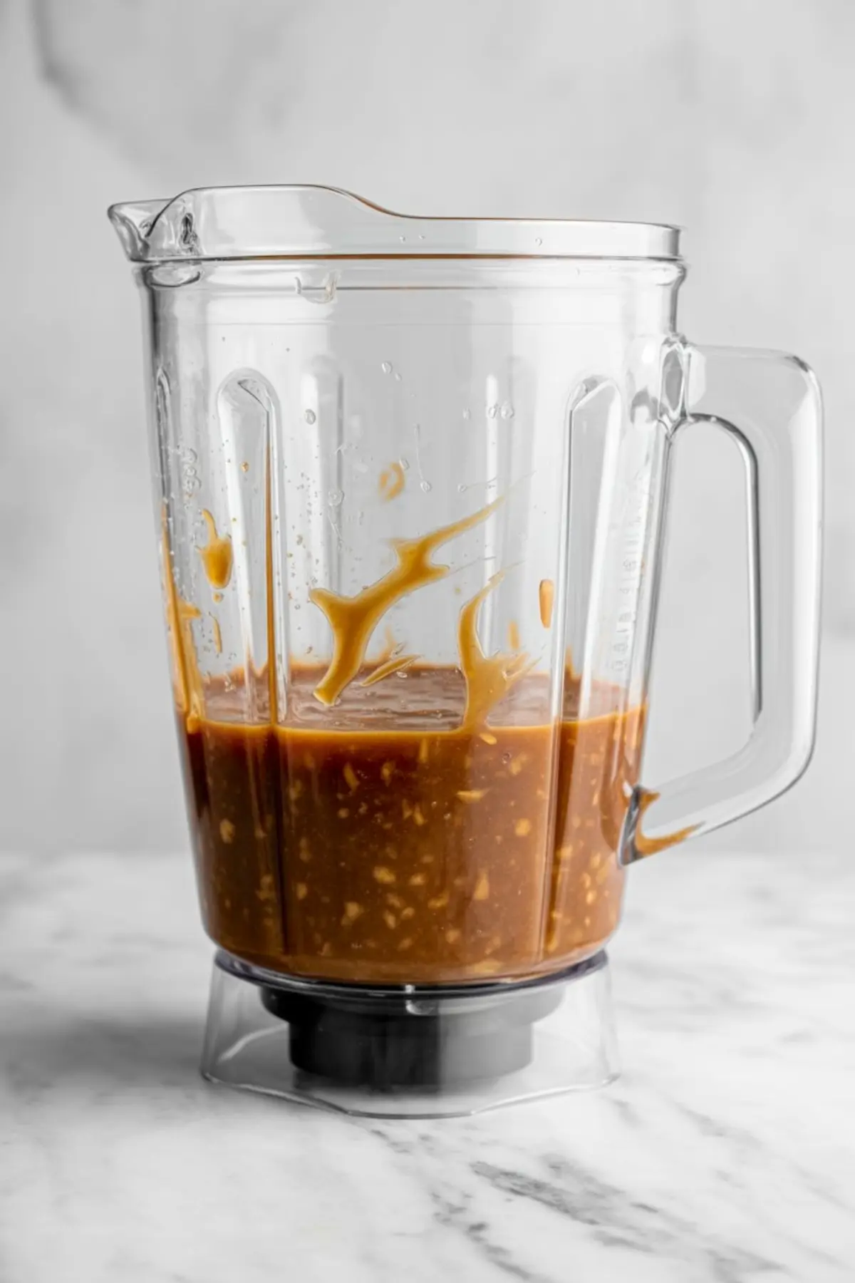 Transparent blender jar partially filled with a blended mixture of dates, plant milk, and vanilla, showcasing the thick texture and small visible date bits.