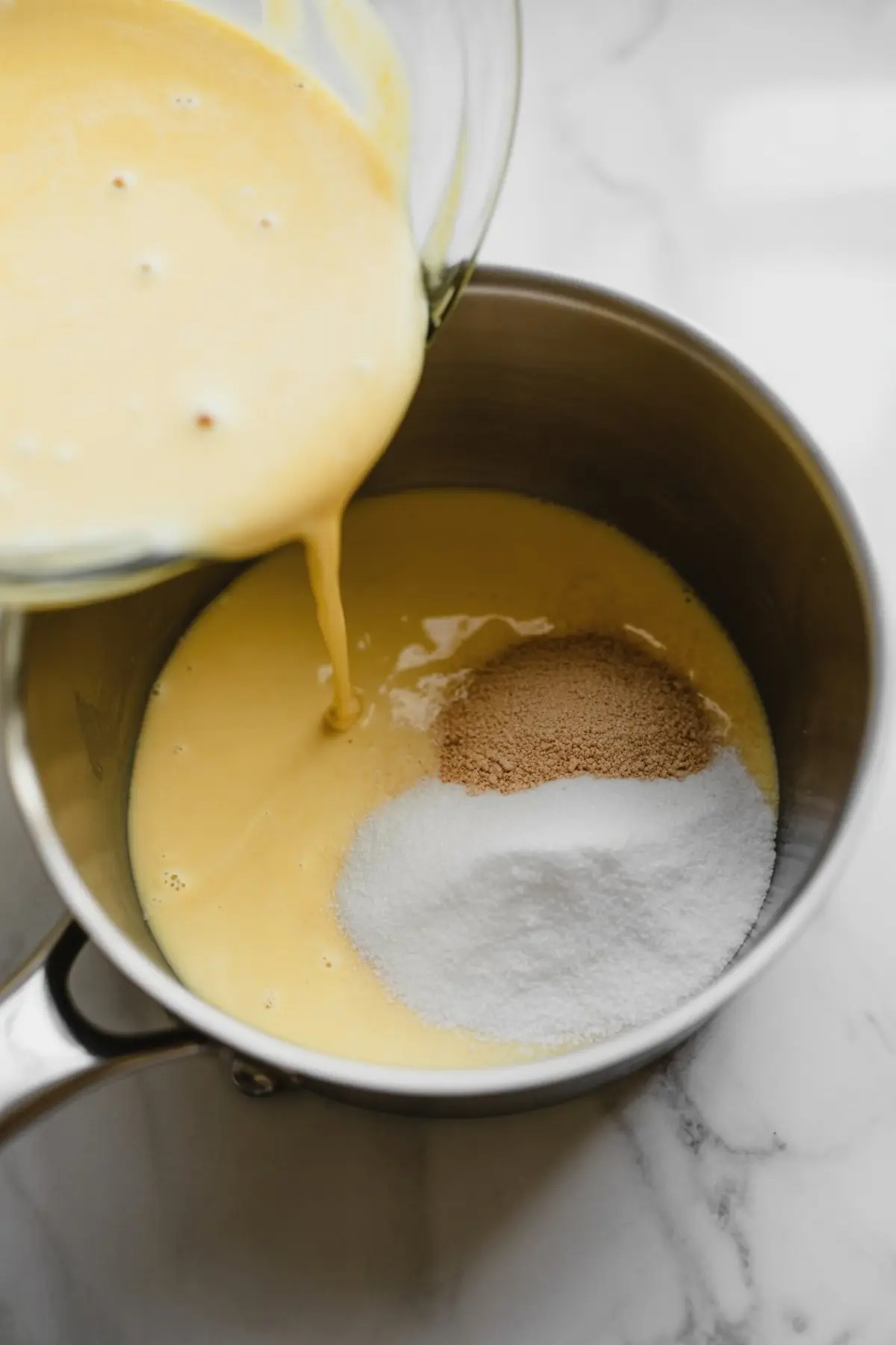 Eggnog mixture being poured into a saucepan over granulated sugar and brown sugar, creating a creamy base for holiday dessert preparation.